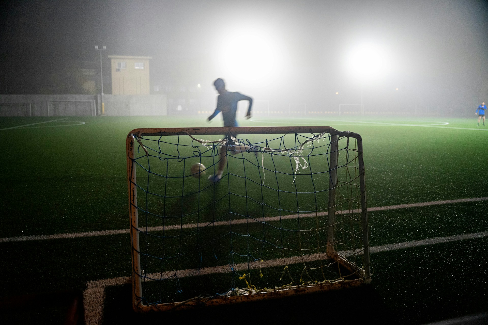A player striking the ball in front of a goal under floodlights